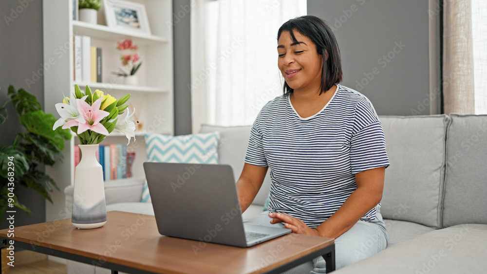 A hispanic woman enjoys browsing on a laptop in her cozy living room, highlighting modern lifestyle and freelance work. A hispanic woman enjoys browsing on a laptop in her cozy living room, highlighting modern lifestyle and freelance work.