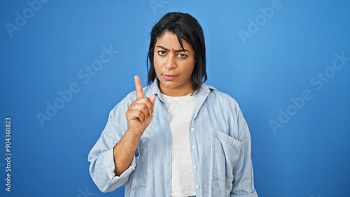 A hispanic woman in casual attire gestures warningly against a blue background. photo