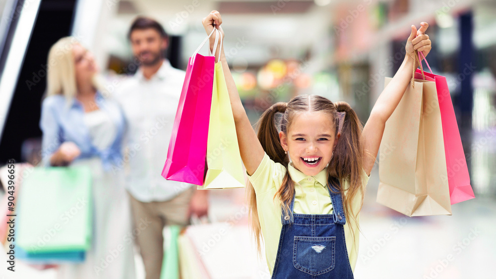 Great Shopping. Excited Girl Holding Shopper Bags Walking With Parents In Mall Center. Selective Focus Great Shopping. Excited Girl Holding Shopper Bags Walking With Parents In Mall Center. Selective Focus