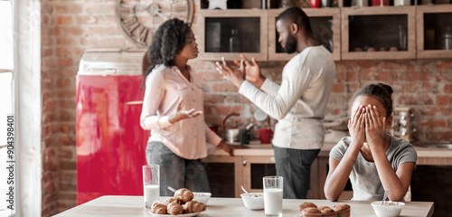 Family problems concept. African american little girl covering her eyes with hands, parents figting during breakfast, copy space photo