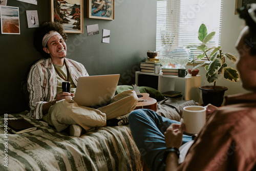 Tableau sur toile Curly-haired student sitting with laptop on bed and loathing out loud while his