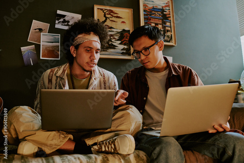 Biracial programmers sitting on bed while discussing technical problems and trying to solve them together photo