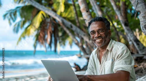 An older man with glasses and a light-colored shirt is sitting by the beach, working on his laptop under the shade of palm trees, enjoying the serene tropical environment.