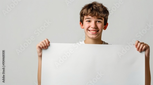 A cheerful boy with tousled hair holds a blank sheet of paper against a neutral background, smiling brightly. Ideal for promotional content or educational materials. photo