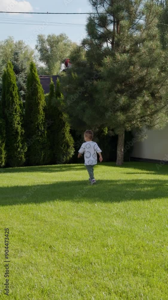 Kid wearing long t-shirt runs outdoors by the green grass. Baby boy enjoying summer time. Vertical video. Kid wearing long t-shirt runs outdoors by the green grass. Baby boy enjoying summer time. Vertical video.