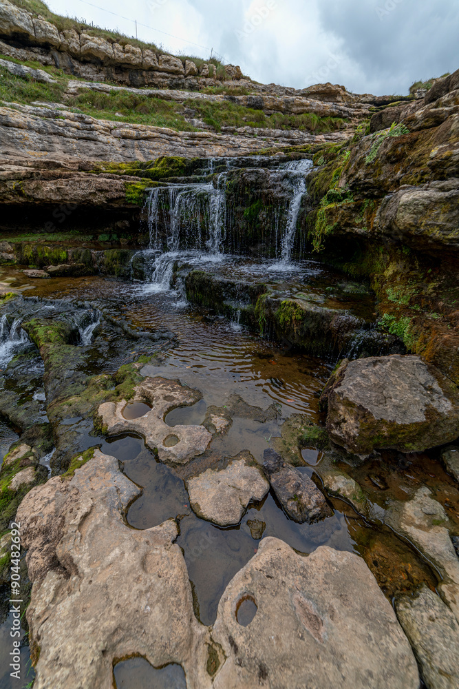 Picturesque waterfall flowing over layered rock formations with lush green moss in Cantabria, Spain. Ideal for nature, travel, and landscape themes. Picturesque waterfall flowing over layered rock formations with lush green moss in Cantabria, Spain. Ideal for nature, travel, and landscape themes.