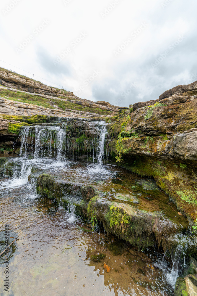 Picturesque waterfall flowing over layered rock formations with lush green moss in Cantabria, Spain. Ideal for nature, travel, and landscape themes. Picturesque waterfall flowing over layered rock formations with lush green moss in Cantabria, Spain. Ideal for nature, travel, and landscape themes.