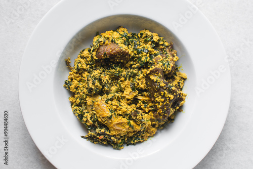 overhead view of Nigerian egusi soup with fish and beef in a white plate, egusi vegetable soup in a large dinner plate, traditional egusi soup in a white dish photo