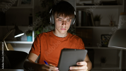 Canvastavla Focused teen boy studying late at night in a home interior, using a tablet and headphones