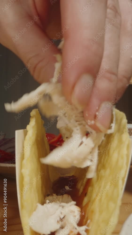 Vertical video. Hand Adds Shredded Chicken to a Taco Shell, Starting the Preparation of a Delicious Taco. Dolly slider, close up. Vertical video. Hand Adds Shredded Chicken to a Taco Shell, Starting the Preparation of a Delicious Taco. Dolly slider, close up.
