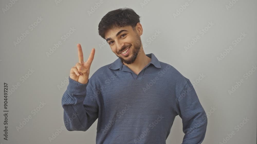 A cheerful young man with beard giving a peace sign against a white background A cheerful young man with beard giving a peace sign against a white background