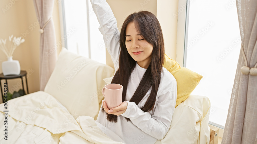 Asian woman enjoying morning in sunny bedroom with coffee mug Asian woman enjoying morning in sunny bedroom with coffee mug
