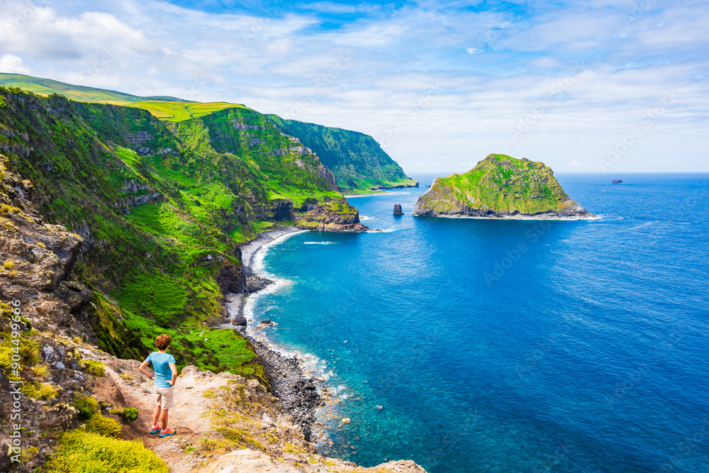Young woman tourist looking at beautiful bay with beach and green cliffs at Baia de Alem, Flores island, Azores, Portugal