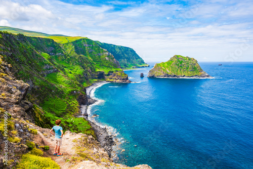 Obraz na płótnie Young woman tourist looking at beautiful bay with beach and green cliffs at Baia de Alem, Flores island, Azores, Portugal w salonie