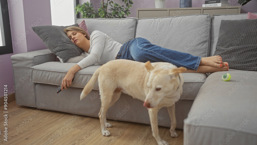 A young woman relaxes on a couch with a dog walking by in a cozy apartment living room. A young woman relaxes on a couch with a dog walking by in a cozy apartment living room.