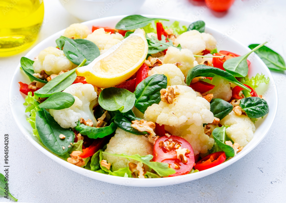 Autumn vegan salad with baked cauliflower and paprika, red tomatoes, baby spinach with walnuts on white background, top view Autumn vegan salad with baked cauliflower and paprika, red tomatoes, baby spinach with walnuts on white background, top view