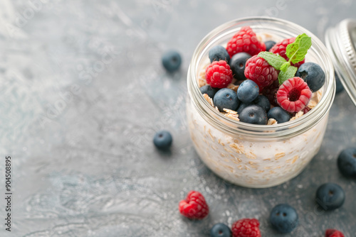Glass jar with overnight oats with fresh strawberries and bilberries on grey background, Healthy vegan vegetarian food, delicious breakfast, snack. Top view