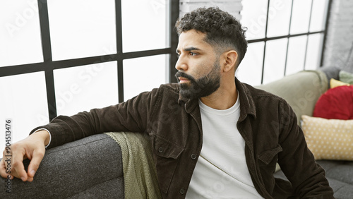 Obraz na plátně Handsome young man with beard sitting thoughtfully in a modern apartment living room