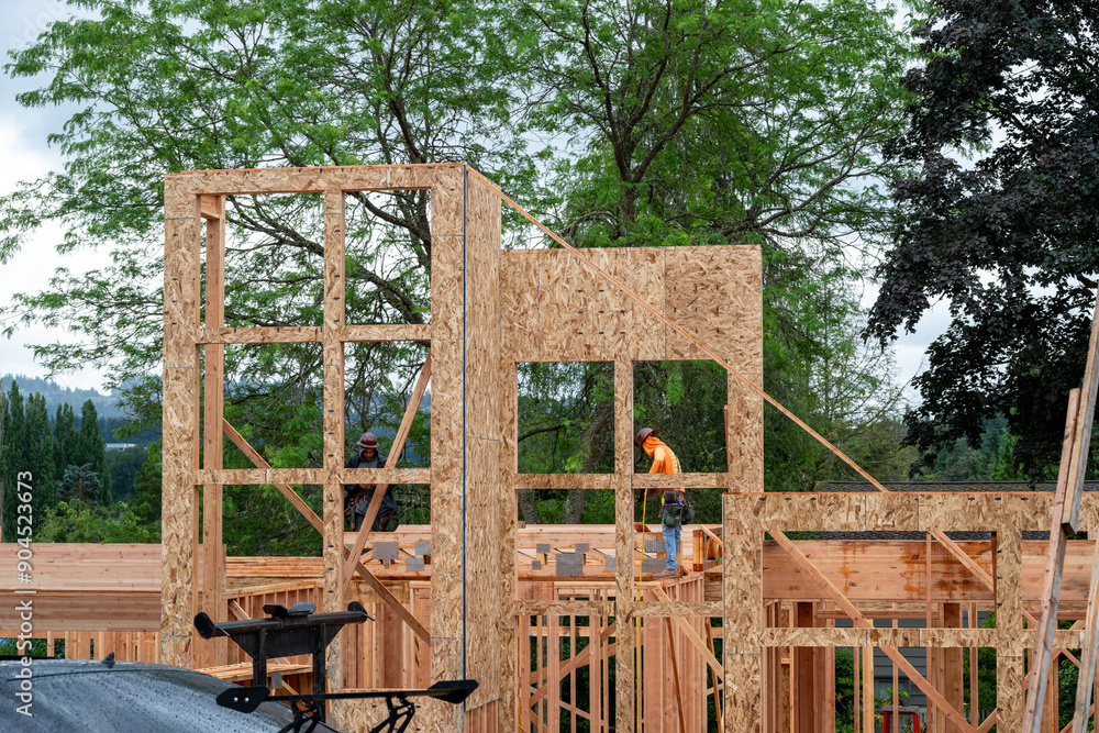 Residential house construction, boom crane lifting lumber delivery, wood support truss beams, workman assisting in placement
Residential house construction, boom crane lifting lumber delivery, wood support truss beams, workman assisting in placement