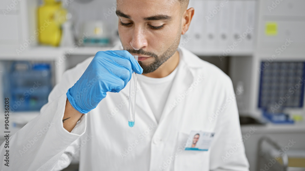 A man smelling a chemical in a test tube inside a laboratory, clad in a lab coat and gloves, concentrating on his research work. A man smelling a chemical in a test tube inside a laboratory, clad in a lab coat and gloves, concentrating on his research work.