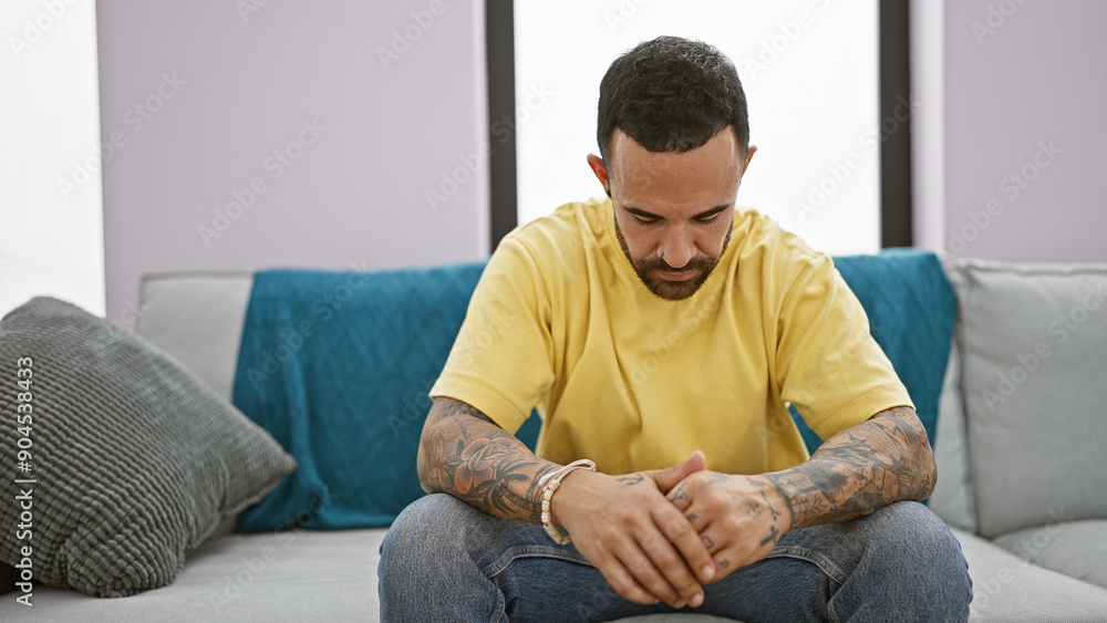 A contemplative tattooed man sits on a couch, his casual appearance and the cozy room creating a relaxed atmosphere. A contemplative tattooed man sits on a couch, his casual appearance and the cozy room creating a relaxed atmosphere.