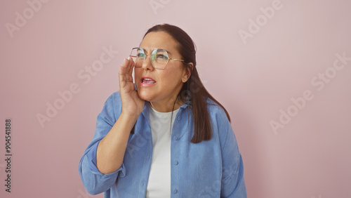 Tablou pe pânză A middle-aged hispanic woman cupping hand to mouth, shouting against a pink isolated background