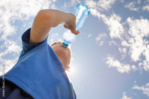 Cuadro en lienzo little boy drinking water from bottle on a hot summer day, thirsty child drinks