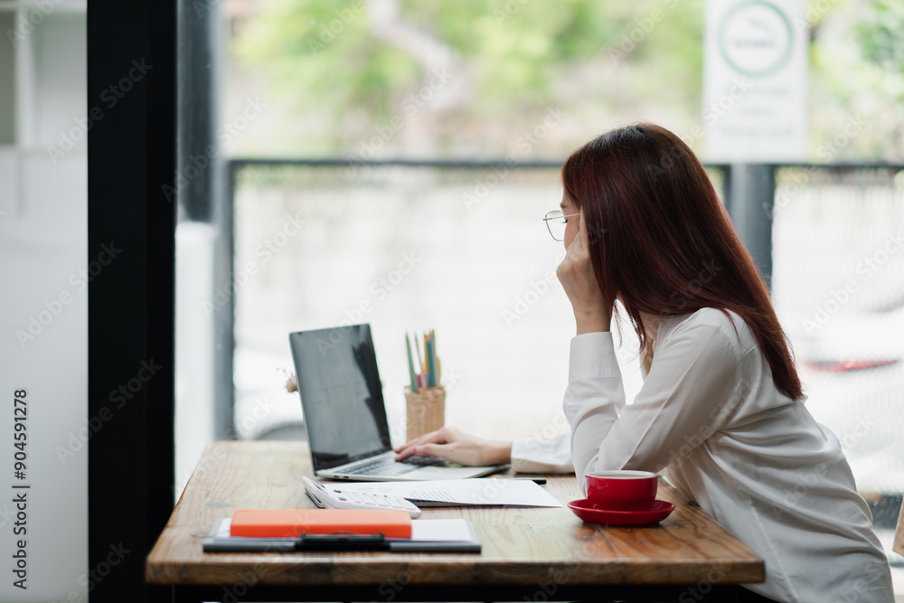 A young woman with glasses working on a laptop at a cozy cafe, surrounded by notebooks and a cup of coffee. A young woman with glasses working on a laptop at a cozy cafe, surrounded by notebooks and a cup of coffee.