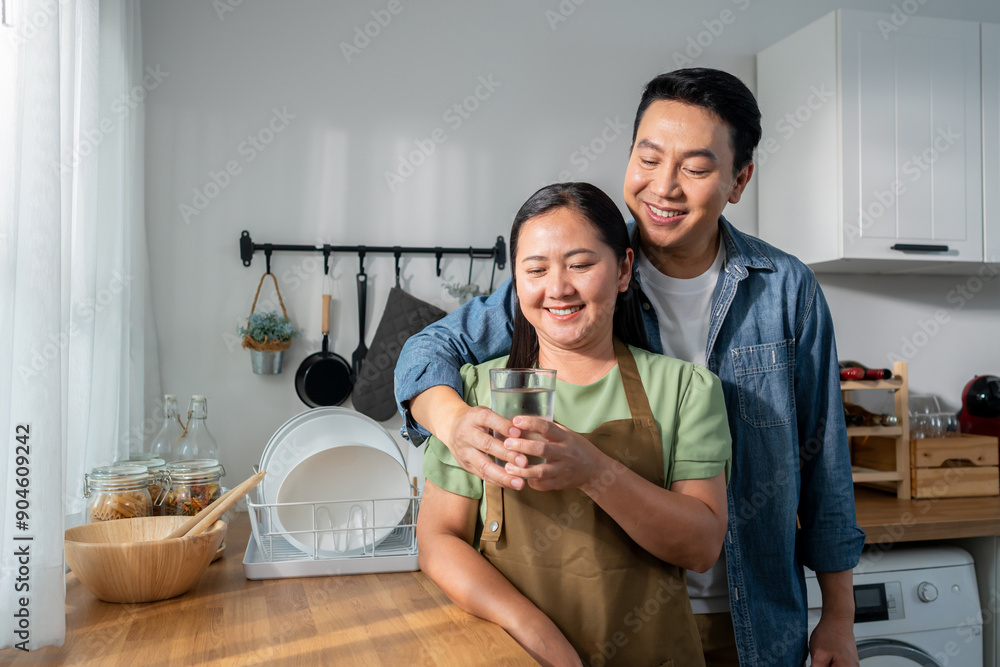 Asian man giving a glass of water to his wife in kitchen room at home. Asian man giving a glass of water to his wife in kitchen room at home.