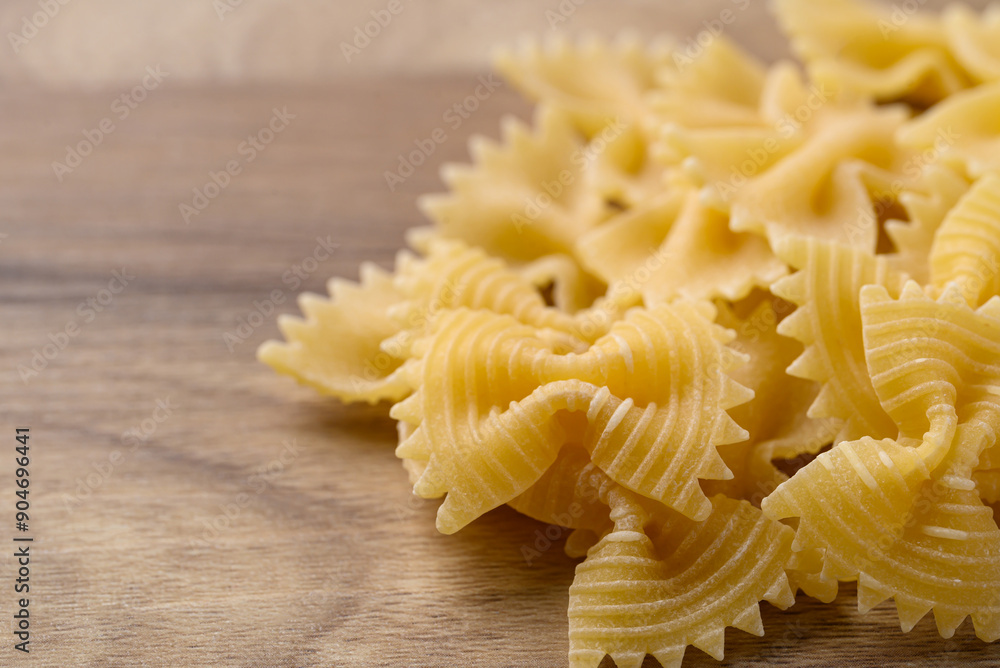 Uncooked farfalle pasta (bow tie shape) on wooden background, Italian food ingredient Uncooked farfalle pasta (bow tie shape) on wooden background, Italian food ingredient