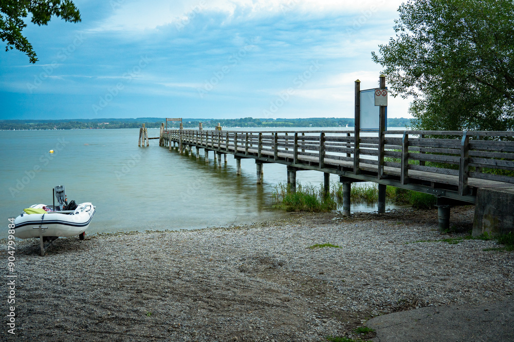 Inflatable boat on the lake shore next to wooden boat dock in Breitbrunn am Ammersee, Bavaria, Germany in the evening light Inflatable boat on the lake shore next to wooden boat dock in Breitbrunn am Ammersee, Bavaria, Germany in the evening light