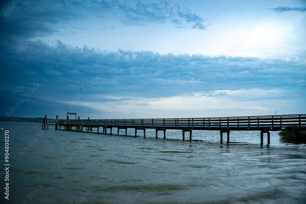 Wooden boat dock in Breitbrunn am Ammersee, Bavaria, Germany in the evening light as a storm approaches. The fleet of the Bavarian lake shipping company includes several steamships on the Ammersee Wooden boat dock in Breitbrunn am Ammersee, Bavaria, Germany in the evening light as a storm approaches. The fleet of the Bavarian lake shipping company includes several steamships on the Ammersee