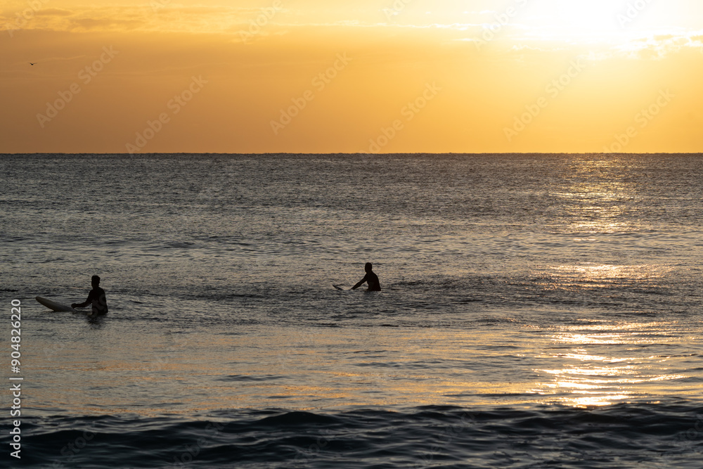 Fototapeta premium Two silhouette surfers at sunrise on there surfboards in the ocean 