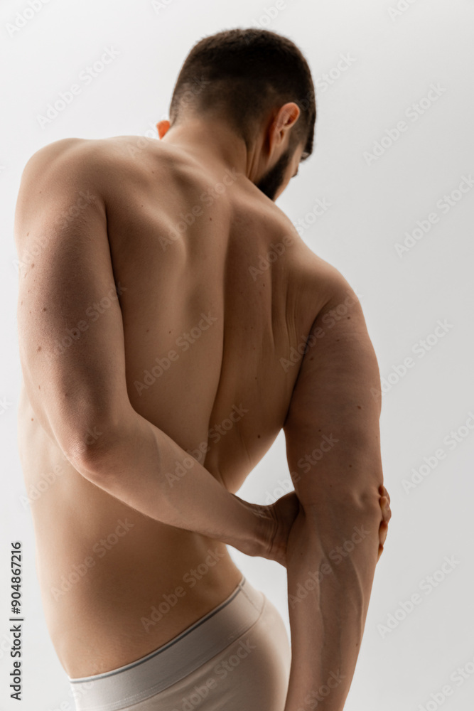 Rear view photo of bearded man in white underwear stands holding hands behind back against white background. Concept of male health, body care, natural beauty people, fitness. Rear view photo of bearded man in white underwear stands holding hands behind back against white background. Concept of male health, body care, natural beauty people, fitness.