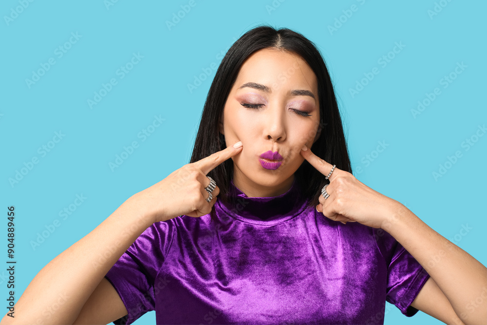 Beautiful Asian woman with applied purple lipstick on blue background Beautiful Asian woman with applied purple lipstick on blue background