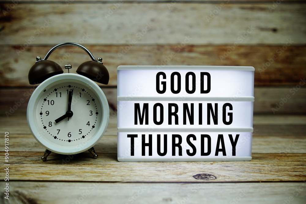 Good Morning Thursday text on LED lightbox with alarm clock on wooden background Good Morning Thursday text on LED lightbox with alarm clock on wooden background