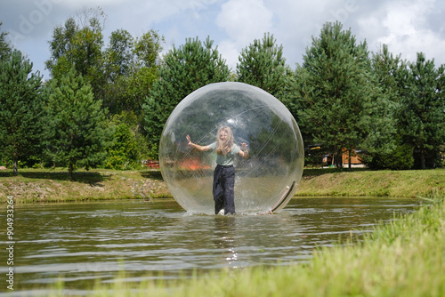 Aqua zorbing on water. A girl in a transparent balloon on the water, lake, nature, forest. Girl inside big inflatable ball having fun, summer activities