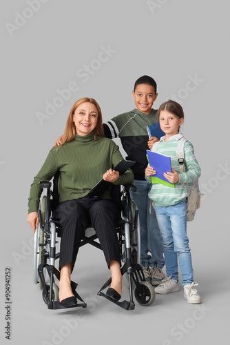 Mature teacher in wheelchair with little pupils on light background