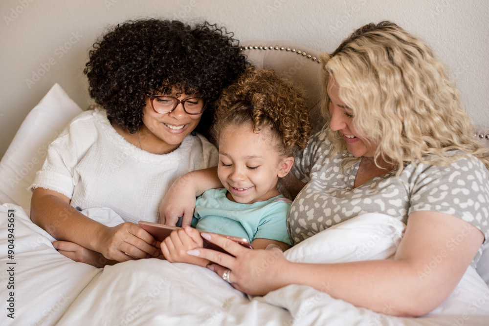 Mother and daughters cuddle in bed smiling looking at a tablet Mother and daughters cuddle in bed smiling looking at a tablet