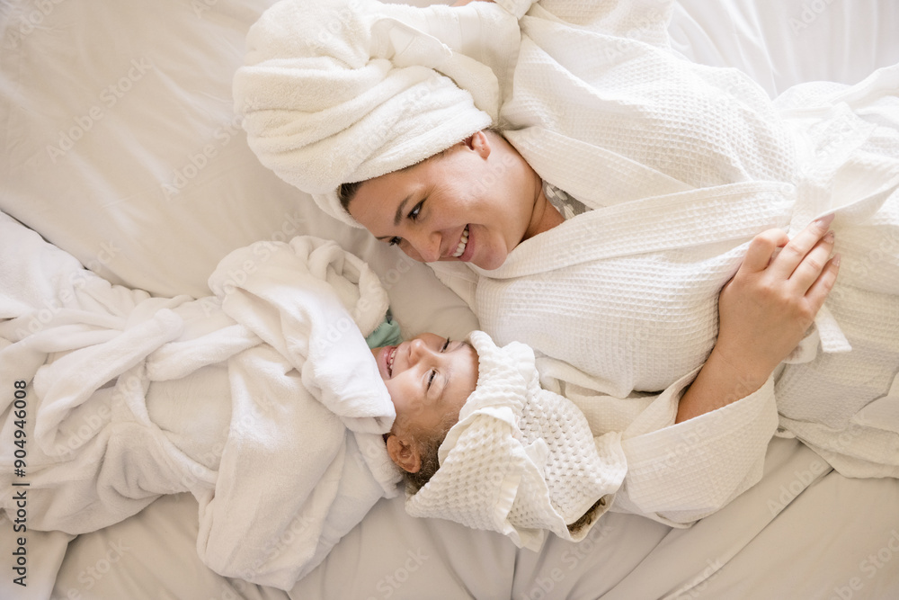 Mother and daughter smiling at each other laying on their back in bed Mother and daughter smiling at each other laying on their back in bed