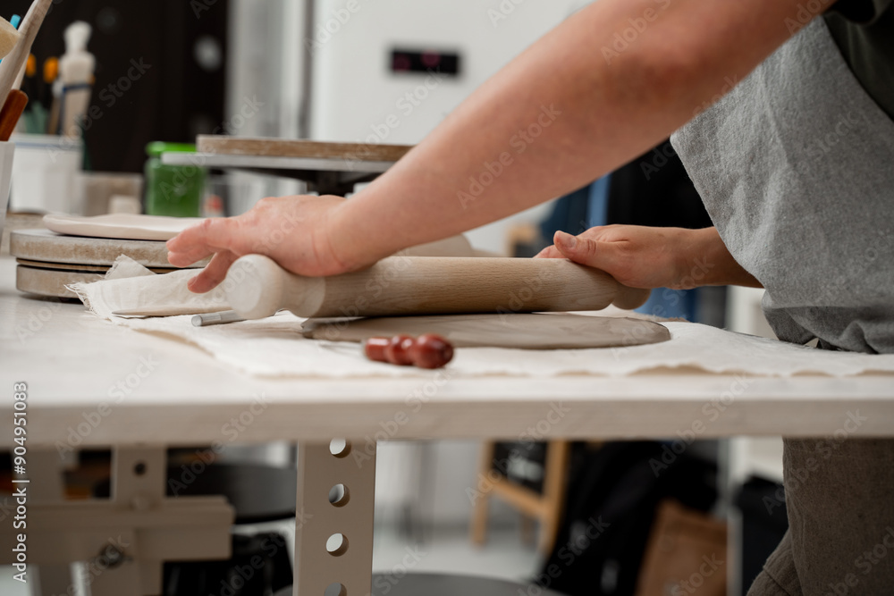 Rolling wooden stick to make flat sheet of clay. Preparing clay for cutting and assembling it. Slab building method in ceramics crafting. Rolling wooden stick to make flat sheet of clay. Preparing clay for cutting and assembling it. Slab building method in ceramics crafting.