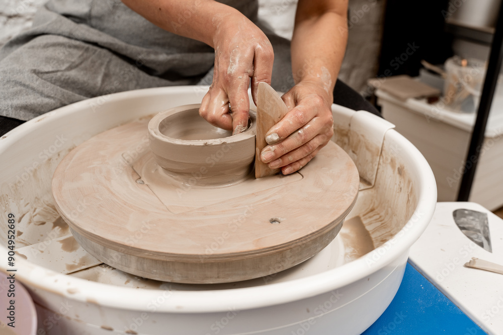 Cutting the lines on sides of a clay product with a wooden scraper. Making smooth edges of pottery with a wooden scraper and a pottery wheel. Cutting the lines on sides of a clay product with a wooden scraper. Making smooth edges of pottery with a wooden scraper and a pottery wheel.