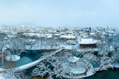 Namwon-si, Jeollabuk-do, South Korea - December 23, 2022: Aerial view of snow covered Ojakgyo Bridge and Gwanghallu Pavilion with pond at Gwanghalluwon Garden against downtown houses 
 photo