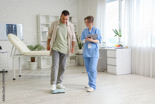 Young man measuring his weight on scales with doctor in clinic