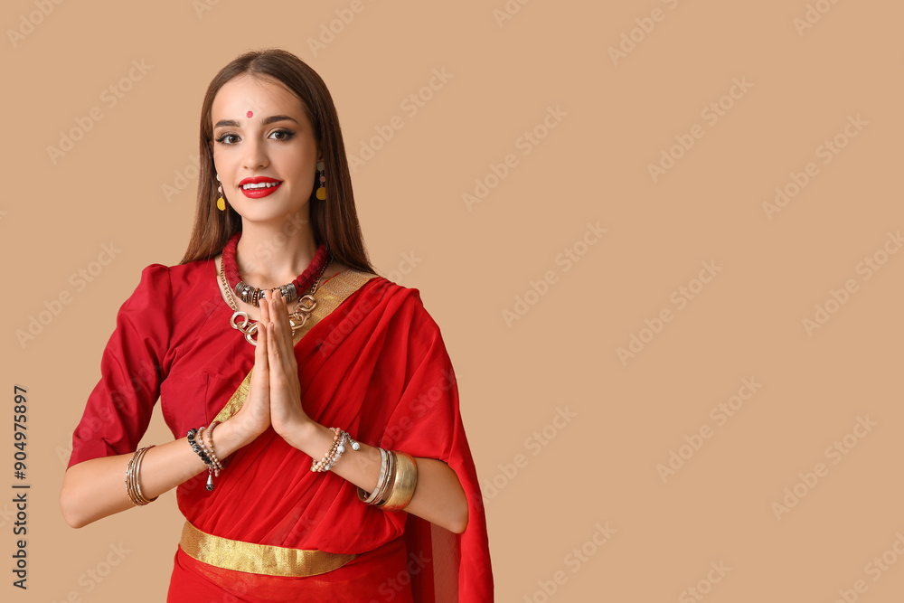 Beautiful young happy Indian woman in sari praying on beige background Beautiful young happy Indian woman in sari praying on beige background