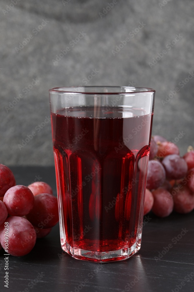 Tasty grape juice in glass and berries on dark textured table, closeup Tasty grape juice in glass and berries on dark textured table, closeup
