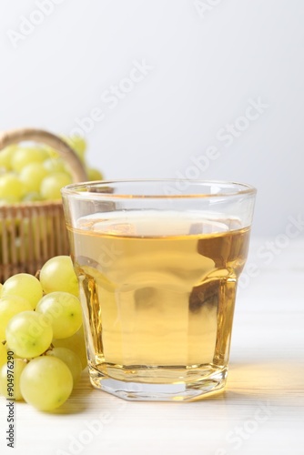 Ripe grapes and glass of tasty juice on white wooden table