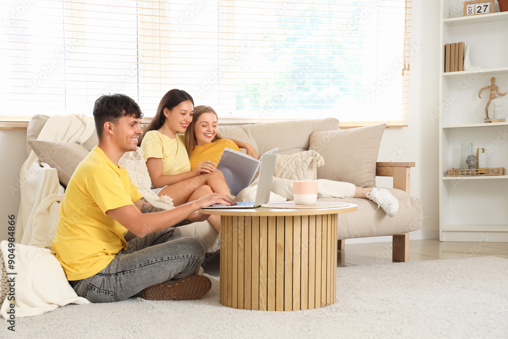 Young man using laptop with two women reading magazine at home. Polyamory concept Young man using laptop with two women reading magazine at home. Polyamory concept