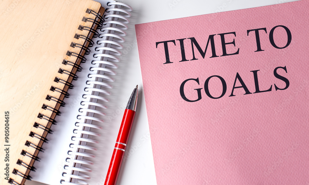 TIME TO GOALS text on pink paper with notebooks TIME TO GOALS text on pink paper with notebooks