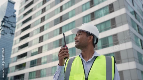 An engineer in a safety helmet and high-visibility vest uses a walkie-talkie at a construction site. photo